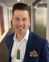 A photo of Al wearing a blue blazer, white shirt and pounamu necklace