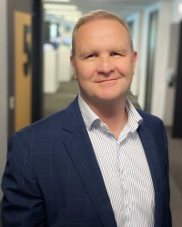 A photo of Chris, a Pākehā man wearing a blue blazer and a striped shirt