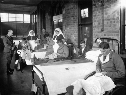 A black and white photo of returned servicemen embroidering in hospital beds, surrounded by nurses